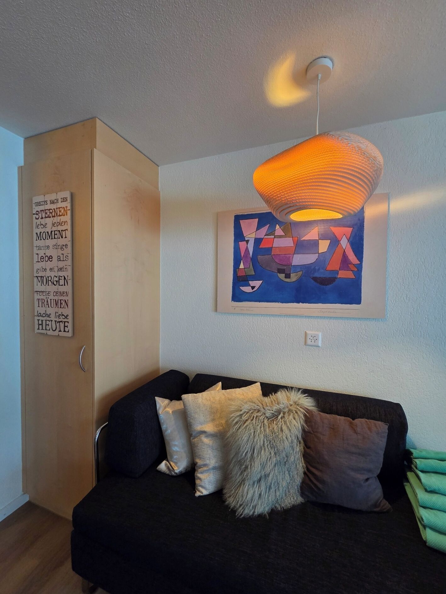 Uma sala de estar moderna com um sofá preto, uma pintura abstrata geométrica e uma luminária pendente.