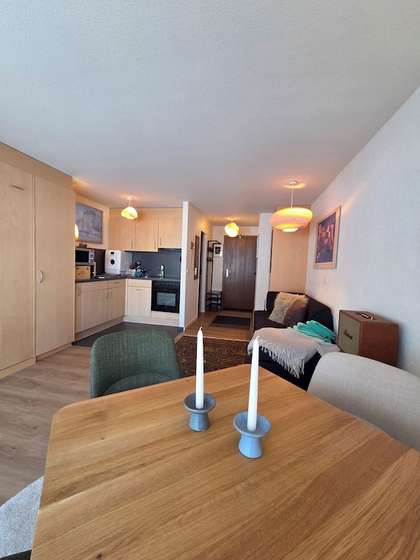 A compact living space with a kitchenette, a dining area with a table and candles, and a seating area with a sofa and a rug.