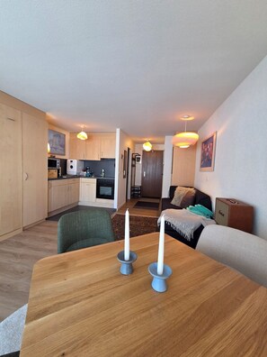 A compact living space with a kitchenette, a dining area with a table and candles, and a seating area with a sofa and a rug.