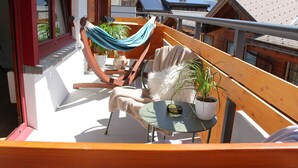 A balcony with a hammock, a chair, a table, and a potted plant. - Cozy studio, centrally located, with mountain views (Saas-Fee)