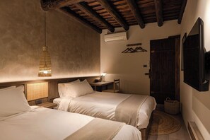 A bedroom with two beds, a hanging light, a bedside table, a chair, a wall-mounted TV, and a door.