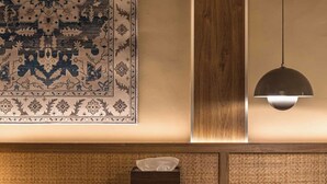 Una mesa de madera con un posavasos tejido, una lámpara colgante y una alfombra estampada en la pared.