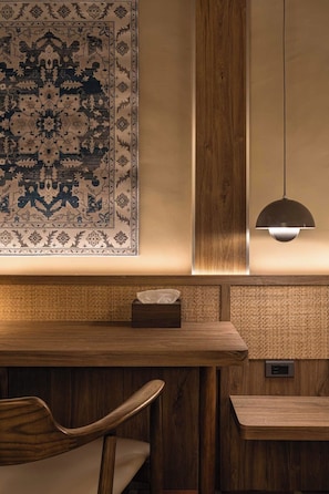 Una mesa de madera con un posavasos tejido, una lámpara colgante y una alfombra estampada en la pared.