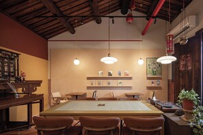 Una habitación tradicional con techo de madera, lámparas colgantes, una mesa central con sillas y una estantería con libros y objetos decorativos.