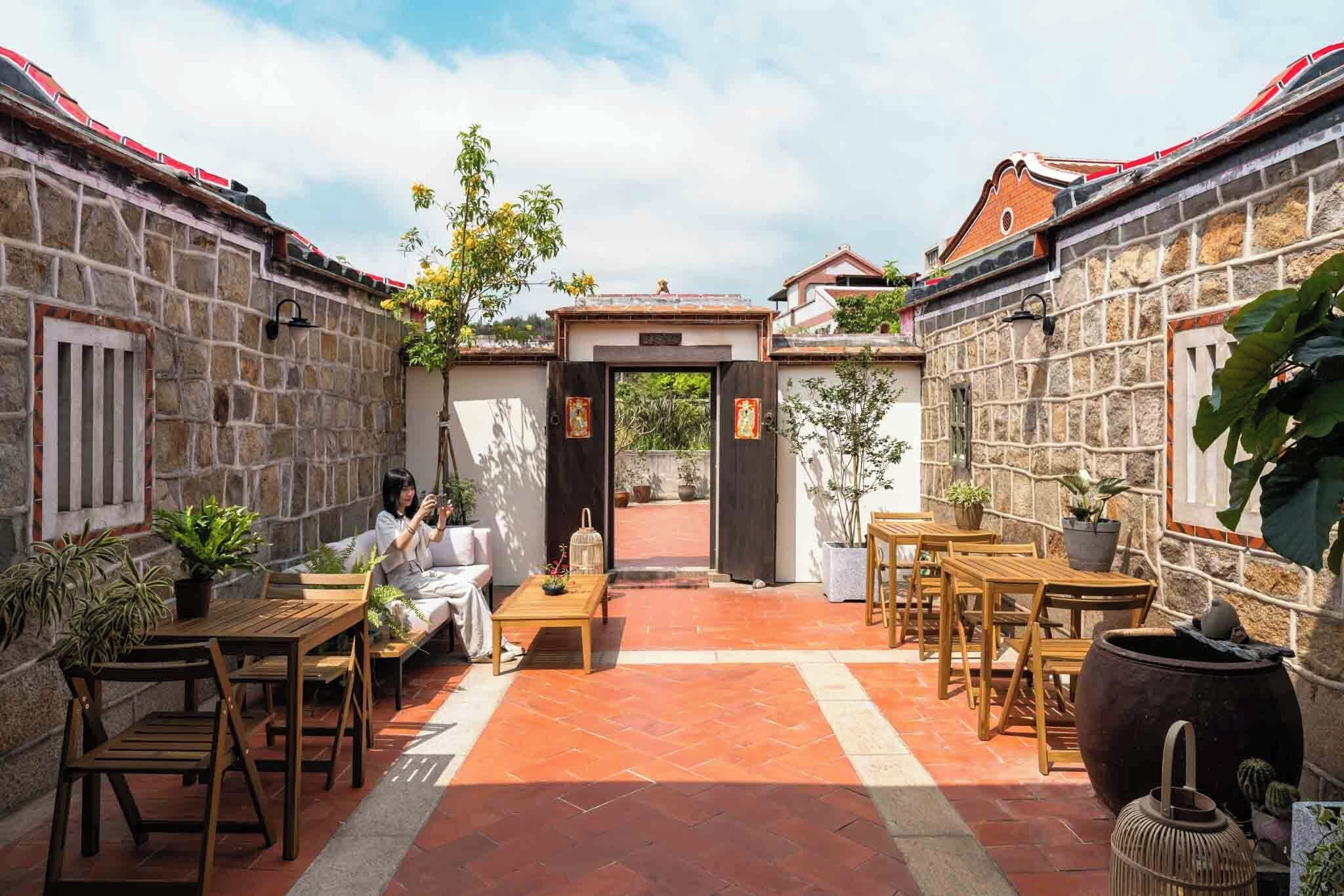 A courtyard with stone walls, a central entrance, outdoor furniture, and potted plants.