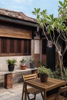 A wooden table and chairs in front of a building with a tiled patio, potted plants, and a bamboo tree.