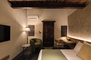 Habitación de hotel con cama, escritorio, silla, lámpara y armario.