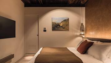 A bedroom with a bed, a painting on the wall, a door, and a hanging light fixture.