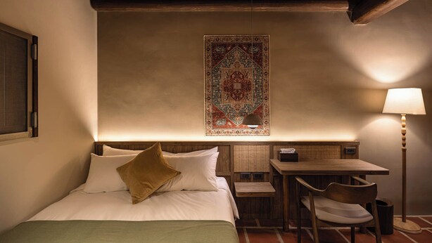 Habitación de hotel con cama, escritorio, silla, lámpara y una alfombra decorativa.