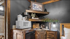 A compact kitchen with a microwave, coffee maker, and a shelf with decorative items. - The Lost Compass (Sautee Nacoochee)