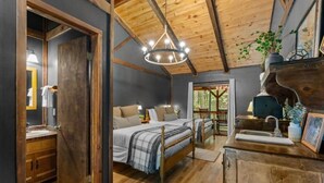 A bedroom with a wooden ceiling, a chandelier, a bed with a plaid blanket, and a wooden dresser with a sink. - The Lost Compass (Sautee Nacoochee)