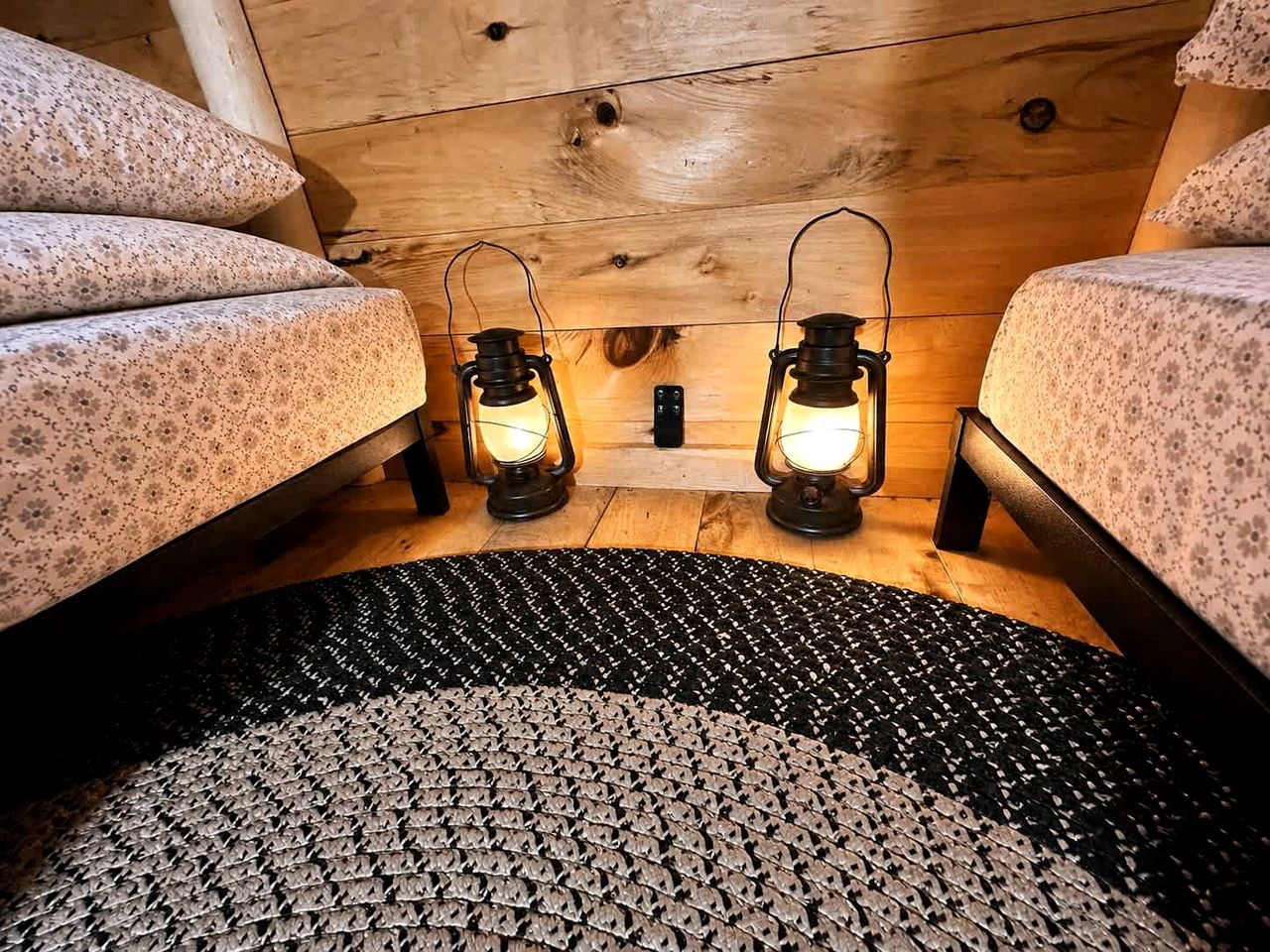A cozy room with two beds, a patterned rug, and two lit lanterns.