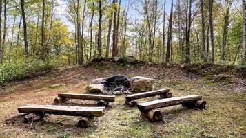 A forest clearing with a fire pit surrounded by logs.