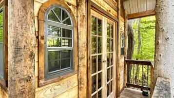 A wooden cabin with a porch, a round window, and a door with glass panels.