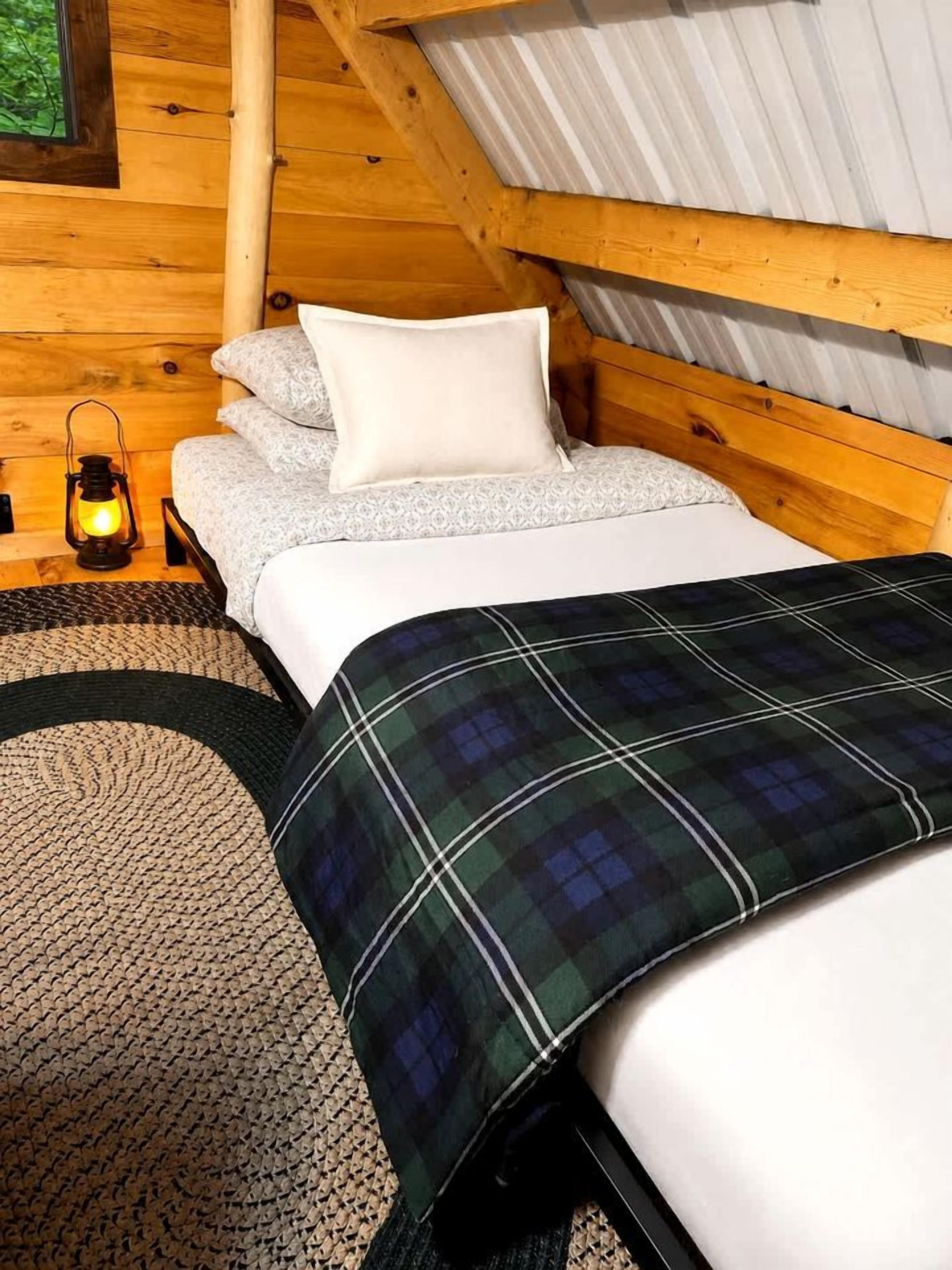 A wooden cabin bedroom with a bed, pillows, a blanket, a lantern, and a woven rug.