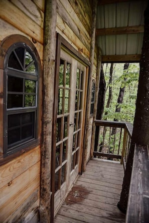 A wooden cabin with a porch, large windows, and a view of the forest.