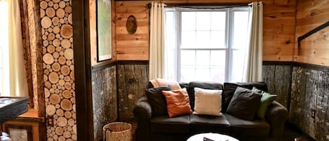 A cozy room with a wooden interior, a leather sofa, a round coffee table, and a window with curtains.