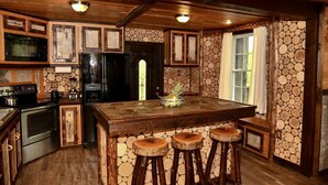 Une cuisine rustique avec un îlot central en bois, des tabourets de bar, un réfrigérateur et un mur en pierre.