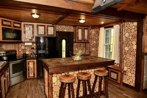 A rustic kitchen with a wooden island, bar stools, a refrigerator, and a stone wall.