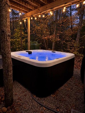 Een hottub in een bebost gebied, verlicht met lichtslingers erboven.