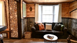 Une pièce chaleureuse avec un décor intérieur en bois, un canapé en cuir, une table basse ronde et une fenêtre avec des rideaux.