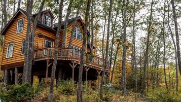 A wooden cabin with a balcony, surrounded by trees.