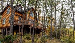 A wooden cabin with a balcony, surrounded by trees.