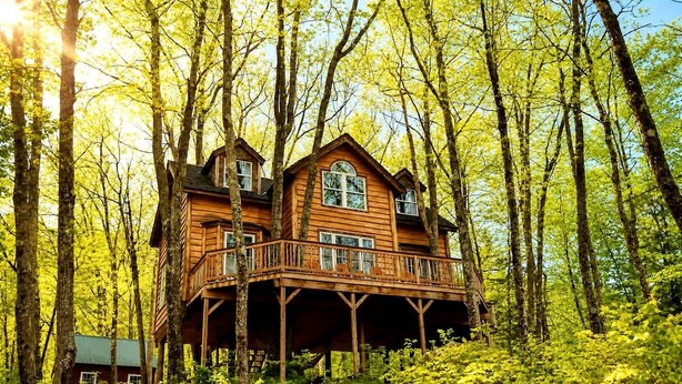 Une cabane en bois dotée d’un balcon, entourée d’arbres.
