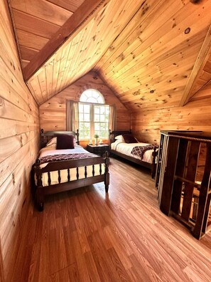 Een slaapkamer in een houten blokhut met schuine wanden, twee bedden en een raam.