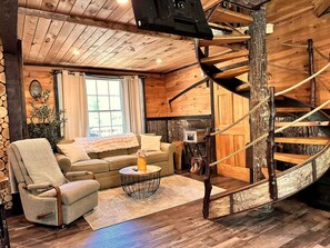 A cozy cabin interior with a wooden staircase, a sofa, a chair, and a coffee table. - Luxury Treehouse with Soaking Tub near White Mountain National Forest, Stoneham, Maine (Stoneham)