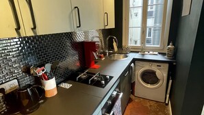 A compact kitchen with a black countertop, a built-in washing machine, and a window with a view of buildings. - Parisian apartment on courtyard (Paris)