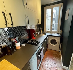 A compact kitchen with a black countertop, a built-in washing machine, and a window with a view of buildings. - Parisian apartment on courtyard (Paris)