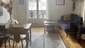 A living room with a dining area, a sofa, a coffee table, and a window with a view of buildings. - Parisian apartment on courtyard (Paris)