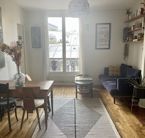 A living room with a dining area, a sofa, a coffee table, and a window with a view of buildings. - Parisian apartment on courtyard (Paris)