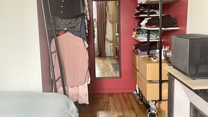A narrow room with a wooden floor, a bed, a wardrobe, a mirror, and a mounted deer head. - Parisian apartment on courtyard (Paris)