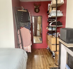 A narrow room with a wooden floor, a bed, a wardrobe, a mirror, and a mounted deer head. - Parisian apartment on courtyard (Paris)
