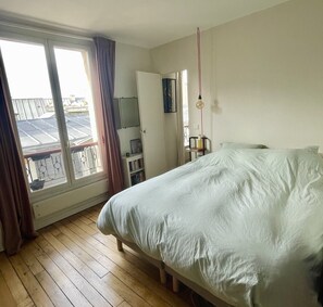 A bedroom with a bed, a wardrobe, a desk with a chair, and a window with curtains. - Parisian apartment on courtyard (Paris)