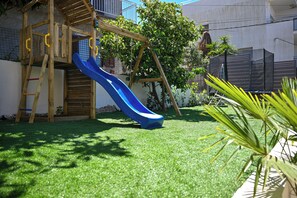 A wooden play structure with a blue slide in a backyard with artificial grass and a tree. - Luxury Villa Blu with pool by the beach (Okrug Gornji)