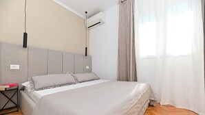 A bedroom with a bed, a nightstand, an air conditioning unit, and a window with curtains. - Luxury Villa Blu with pool by the beach (Okrug Gornji)