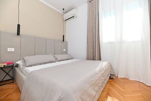 A bedroom with a bed, a nightstand, an air conditioning unit, and a window with curtains. - Luxury Villa Blu with pool by the beach (Okrug Gornji)