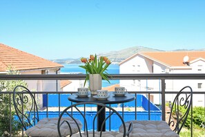 Un balcon avec une table préparée pour le thé, un vase rempli de fleurs et une vue sur la mer et les bâtiments.