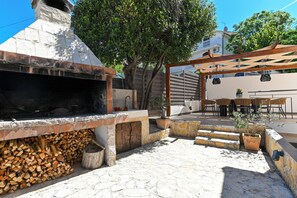 An outdoor patio with a stone fireplace, a wooden pergola, and a seating area with tables and chairs. - Luxury Villa Blu with pool by the beach (Okrug Gornji)