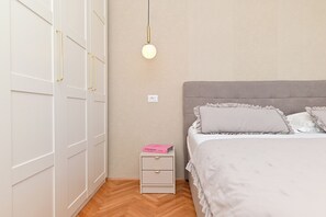 Un dormitorio con cama, mesita de noche, armario y lámpara colgante.