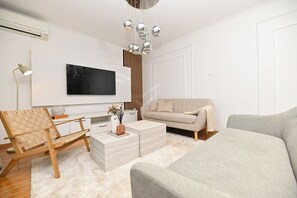 Una sala de estar moderna con televisor de pantalla plana, un sofá, una mesa de centro y una silla de madera.