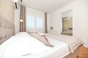 A bedroom with a bed, a bedside table with a vase, and a mirror on the wall. - Luxury Villa Blu with pool by the beach (Okrug Gornji)