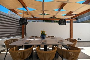 An outdoor dining area with a table set for four, surrounded by wicker chairs, under a shaded pergola. - Luxury Villa Blu with pool by the beach (Okrug Gornji)