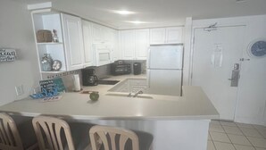 A kitchen with white cabinets, a central island with bar stools, a refrigerator, and a sink.
