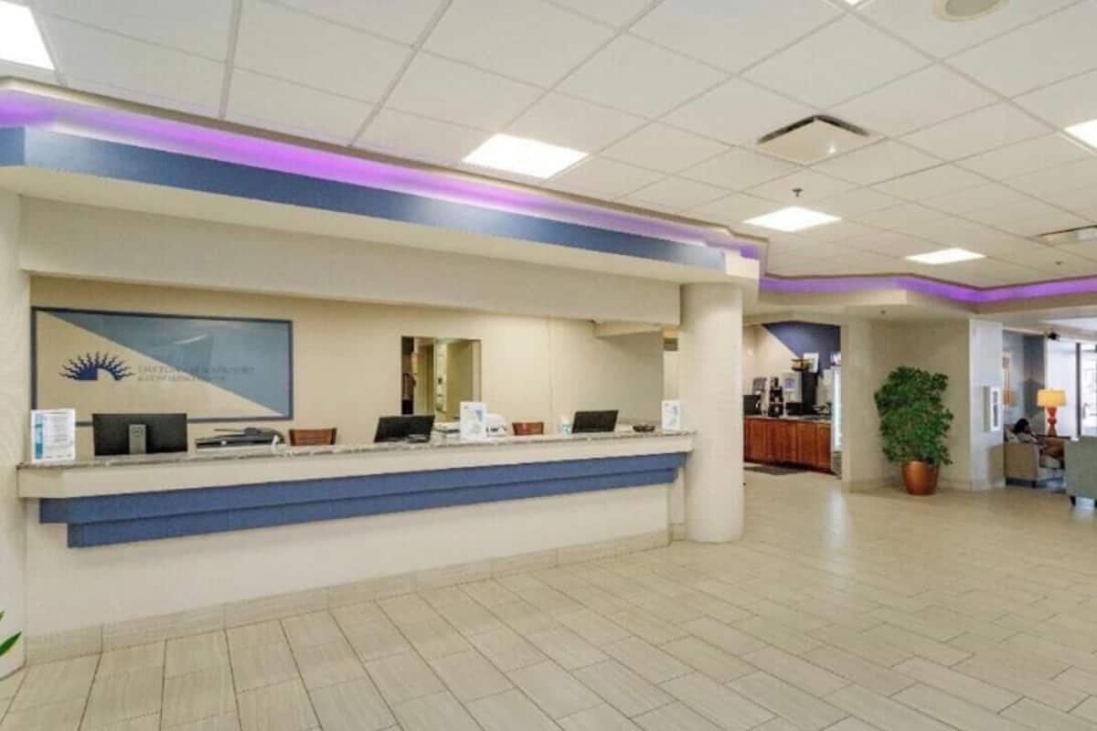 A reception desk with a blue accent, a framed logo, and a potted plant in the background.