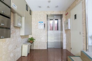 A hallway with a tiled floor, a small trash bin, a potted plant, and a door with a security intercom. - 4th Floor / Shinsaibashi River View / Near Dotonbori, Kuromon Market, and Nipponbashi Station (dotonbori, chuo-ku, osaka)