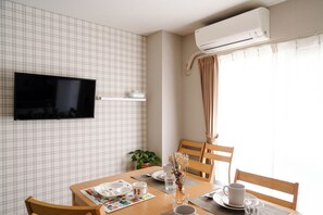 A hotel room with a flat-screen TV mounted on the wall, a dining table with chairs, a potted plant, and an air conditioning unit. - 4th Floor / Shinsaibashi River View / Near Dotonbori, Kuromon Market, and Nipponbashi Station (dotonbori, chuo-ku, osaka)
